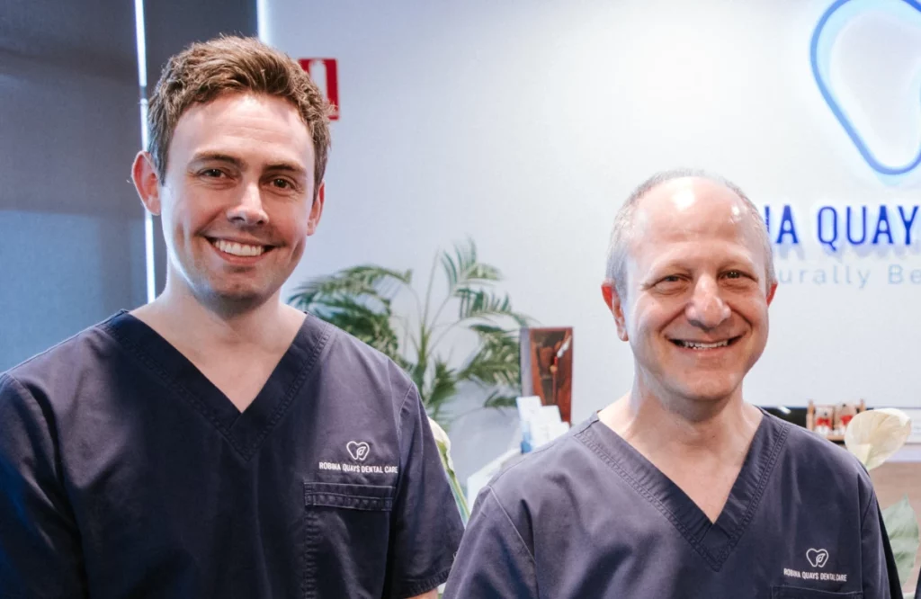 Two male dentists in navy scrubs standing at the Robina Quays Dental Care reception